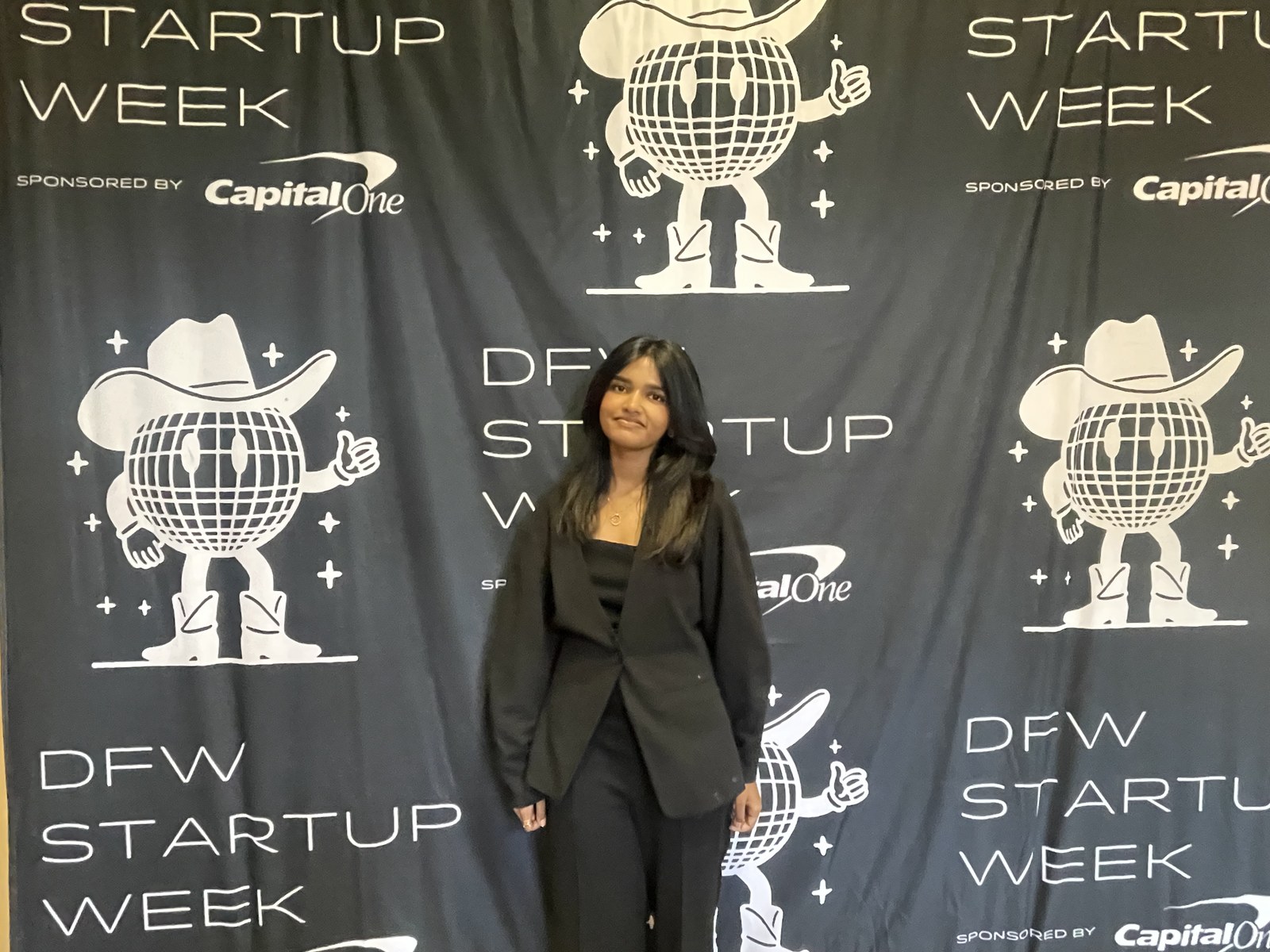 Shruthika Omkumar in a black blazer at DFW Startup Week, Capital One backdrop with a disco-ball cowboy